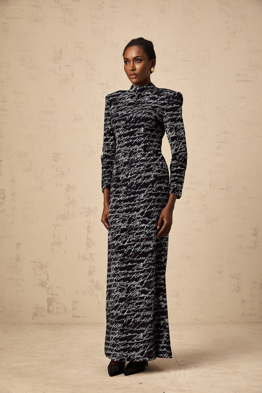 A long black velvet maxi dress with jade colored letter print design adorning the fabric