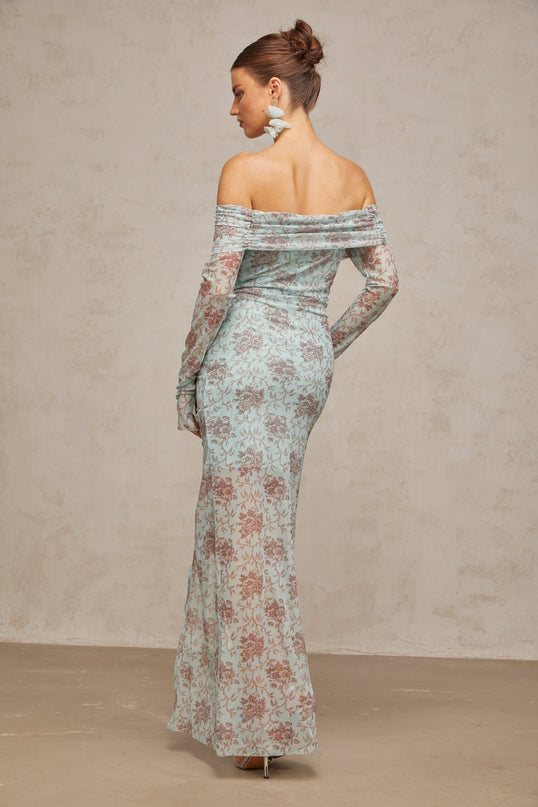 A long blue dress with a floral print pattern and ruched detailing worn by a model standing against a plain background