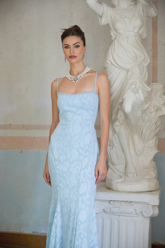 A long blue flared maxi dress with a laceup front and jacquard pattern worn by a model standing against a plain background