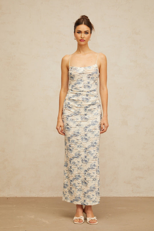 A long blue maxi dress with a textured floral print pattern covering the entire garment featuring an amaryllis flower design