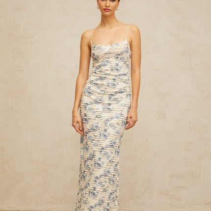 A long blue maxi dress with a textured floral print pattern covering the entire garment The dress features a flowing silhouette and appears to be made of lightweight fabric suitable for warm weather