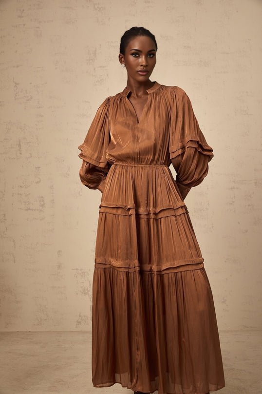 A long brown maxi dress with ruffled trim and multiple tiers worn by a model