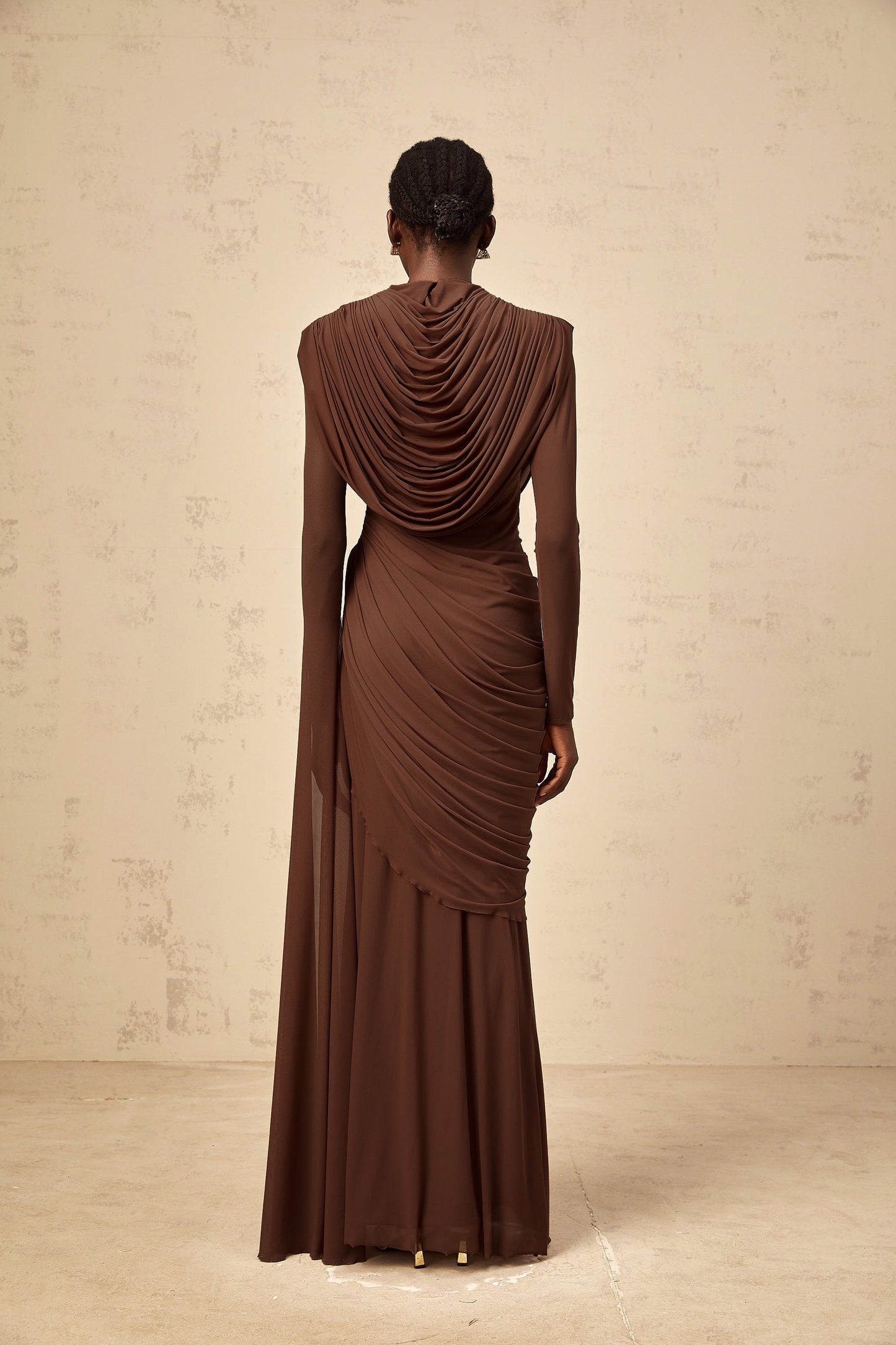 A long brown maxi dress with shirred detailing and draped fabric flowing to the floor