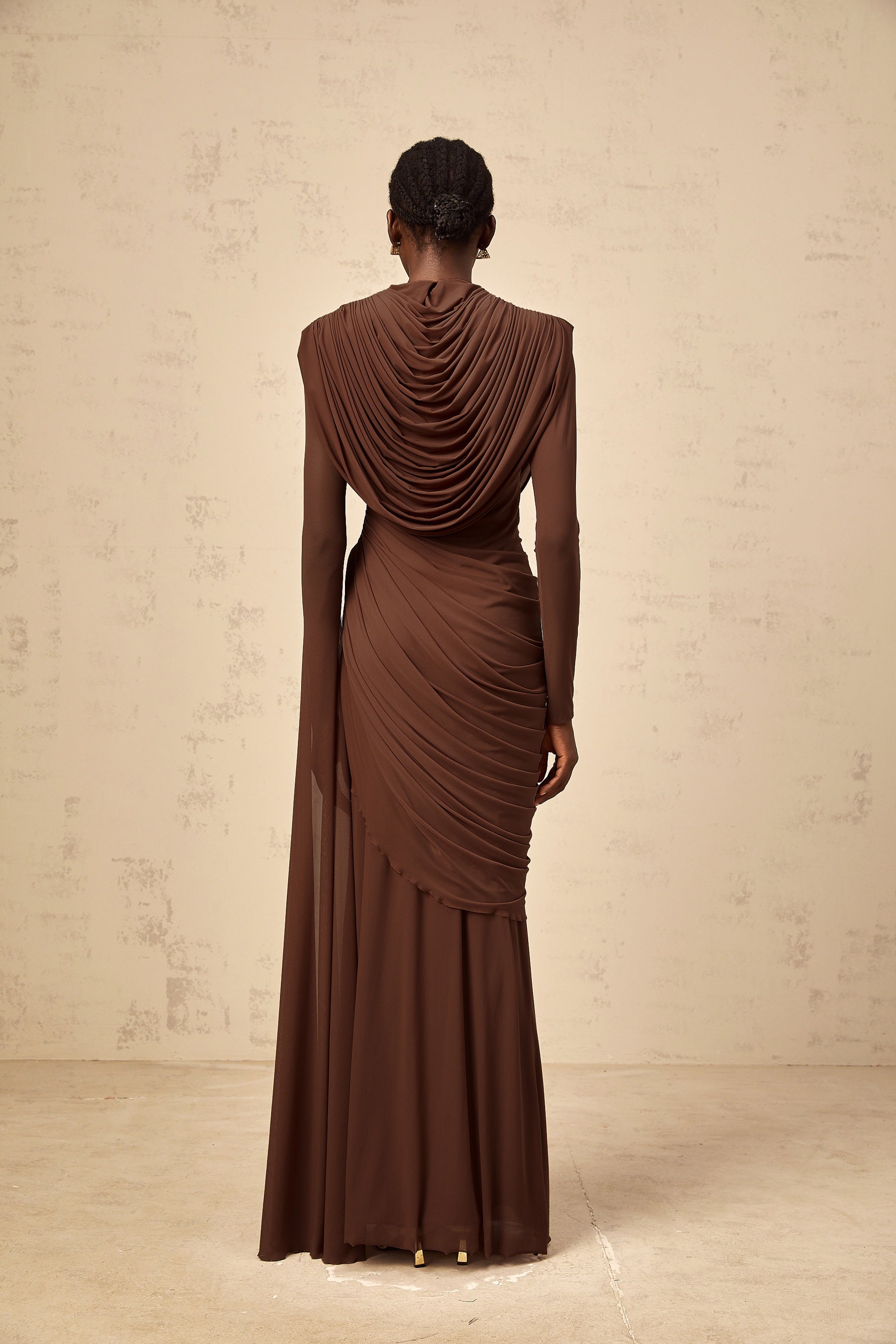 A long brown maxi dress with shirred detailing and draped fabric flowing to the floor