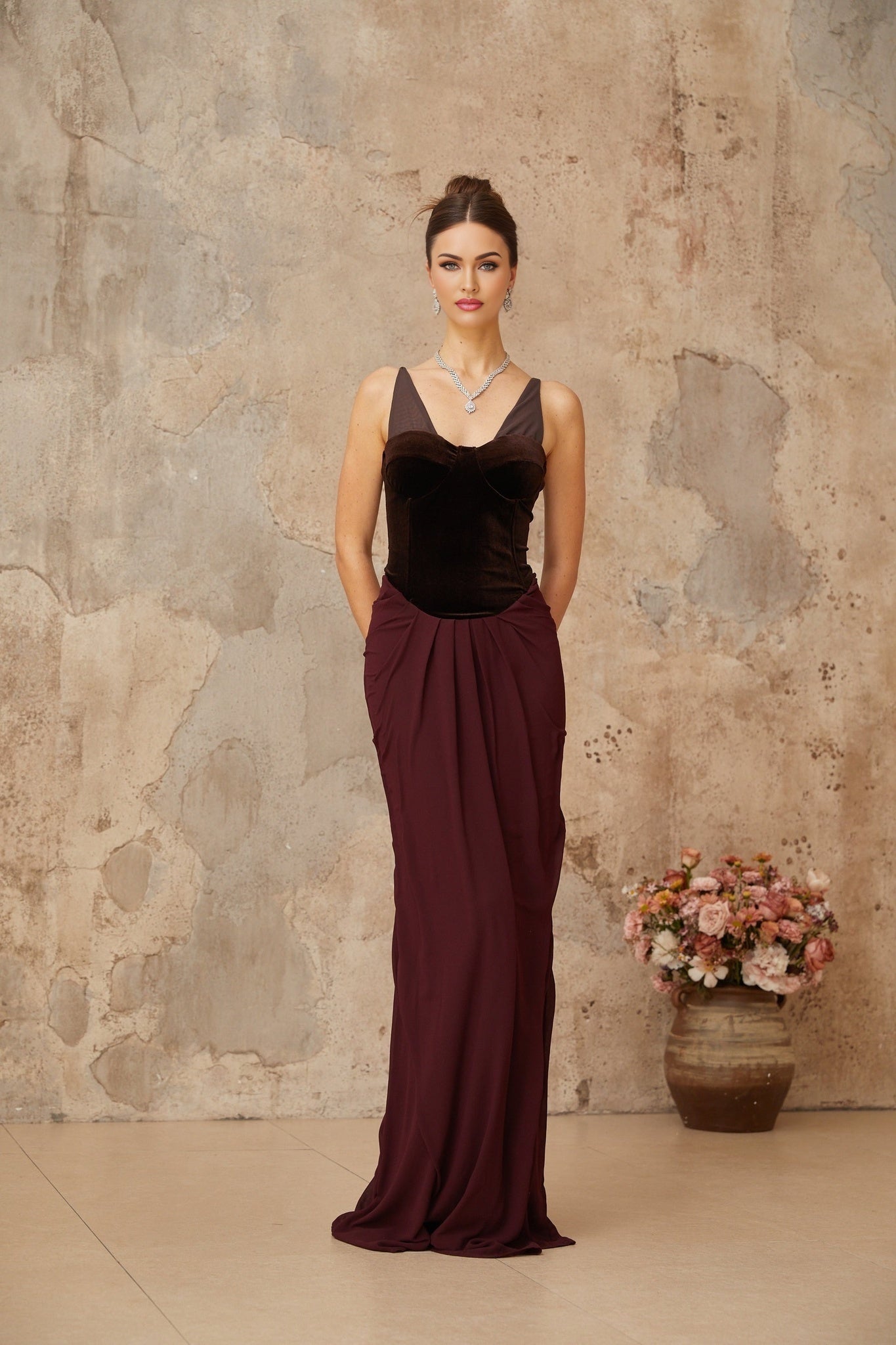 A long burgundy maxi dress with velvet panels and shirred detailing featuring a fitted bodice and flowing skirt