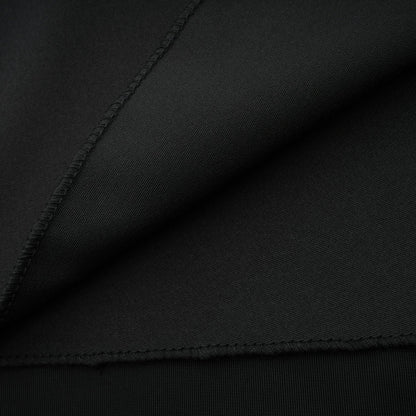 A long dark velvet dress with an open back and embellished details worn by a model standing in an elegant pose