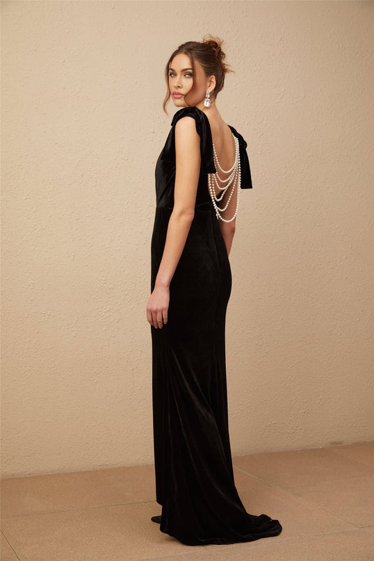 A long dark velvet dress with an open back and embellishments named Audrey worn by a model standing in an elegant pose