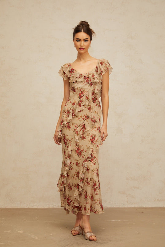 A long floral print maxi dress with ruffles and a flared skirt in light pastel colors against a plain background