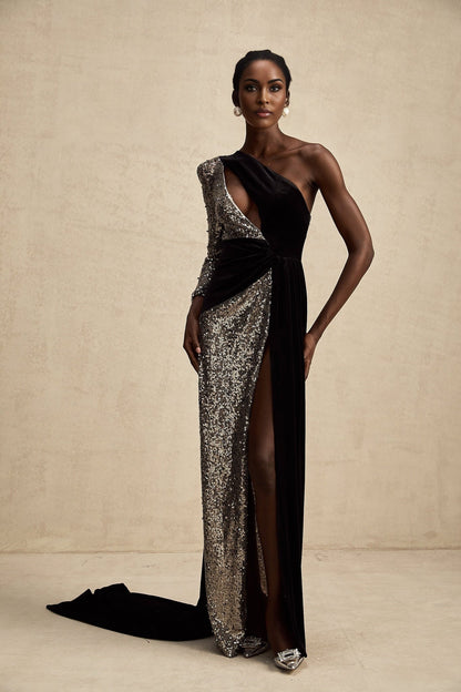 A long flowing asymmetric maxi dress covered in shimmering sequins featuring a oneshoulder design and a high slit