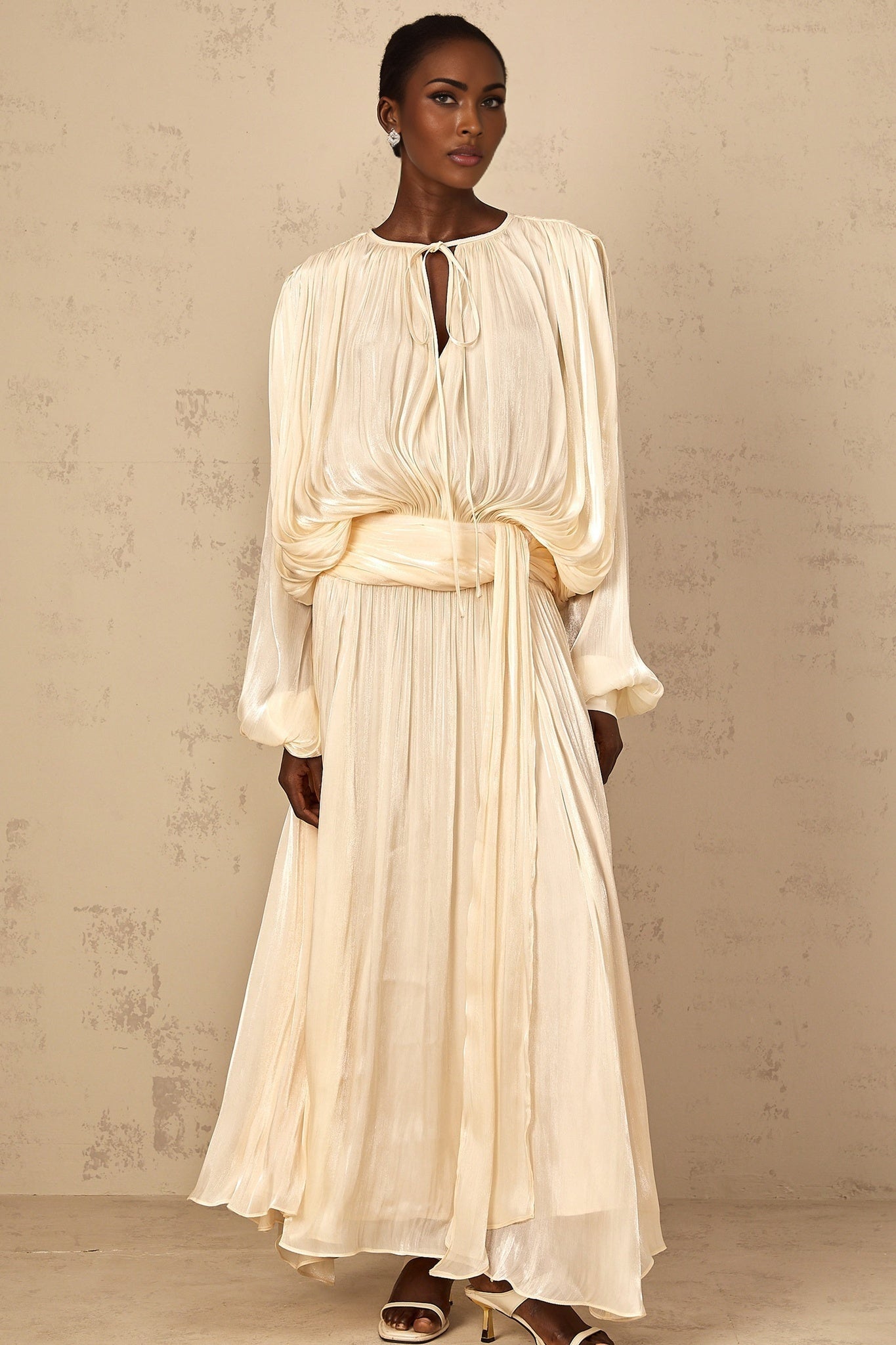 A long flowing maxi dress in a neutral color with pleated ruffles and a feminine silhouette named Eugenie