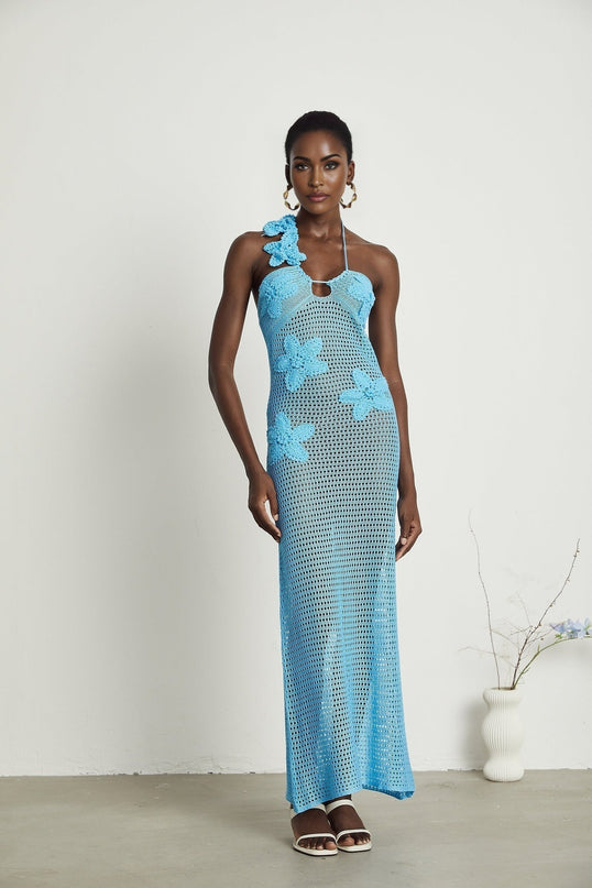 A long flowing maxi dress with crochet detailing and decorative faux flowers sewn onto the fabric creating an intricate floral pattern throughout the garment