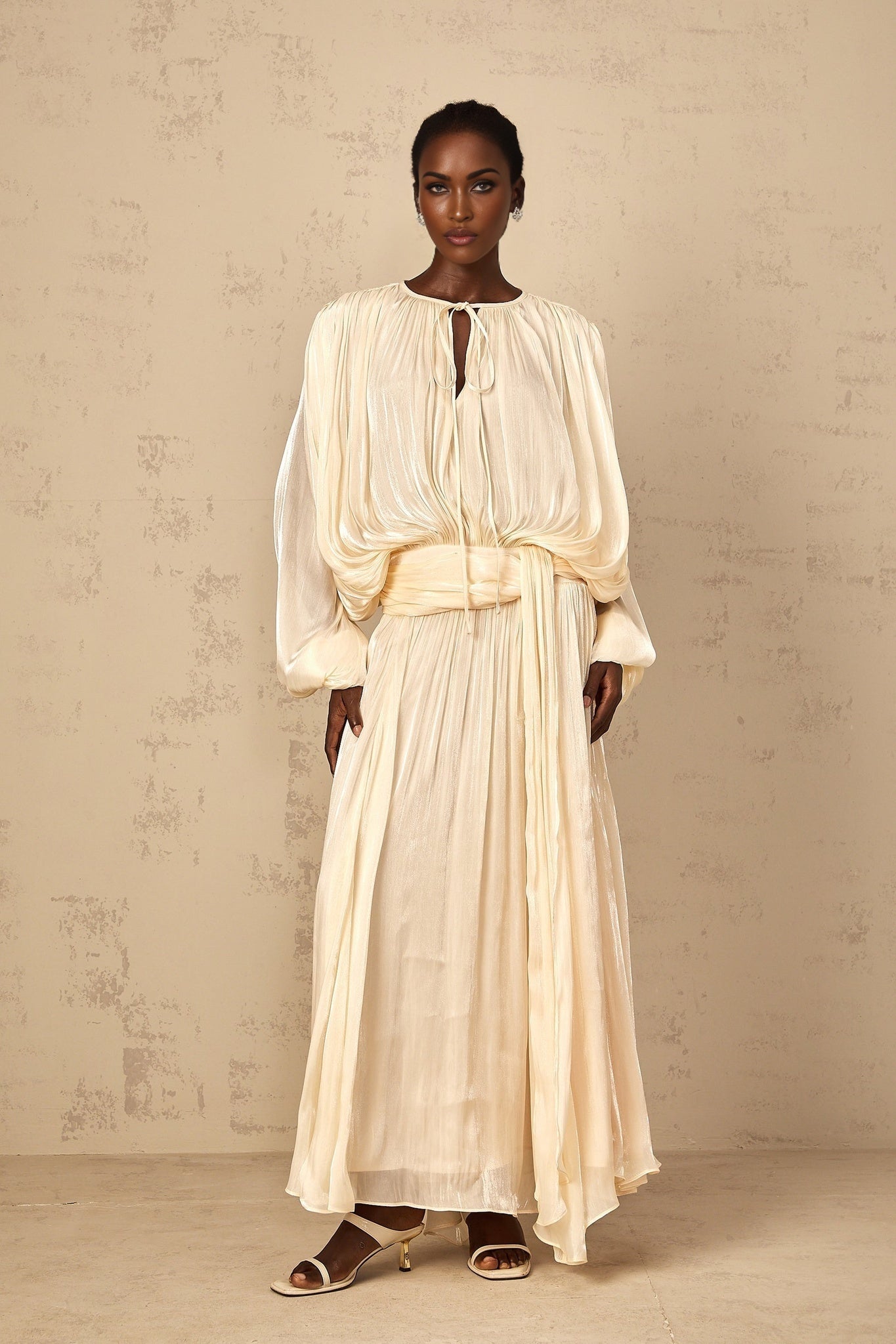 A long flowing maxi dress with pleated ruffle details in a neutral color featuring a feminine silhouette and elegant design