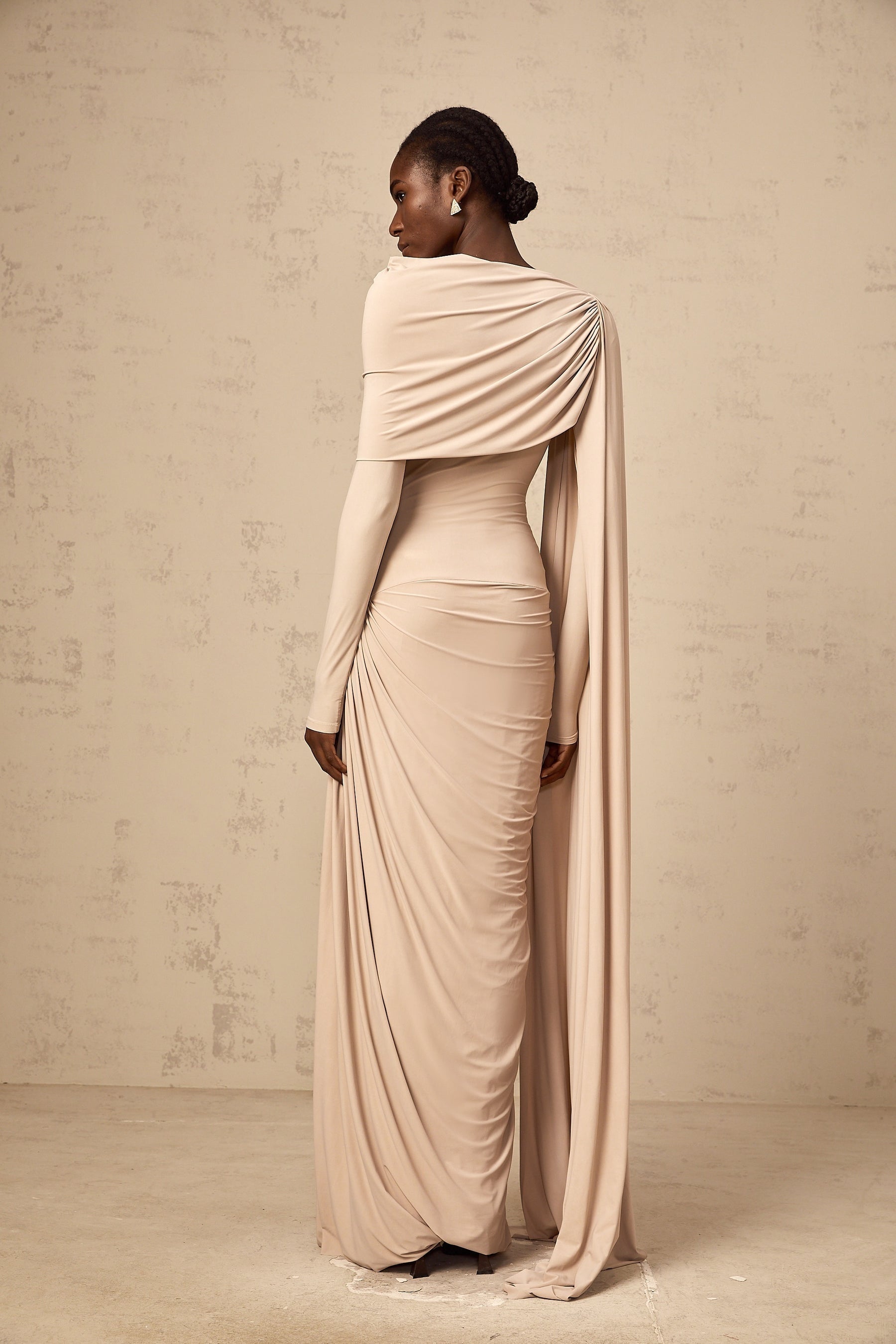 A long flowy maxi dress in neutral tones featuring a draped design and ribbon details