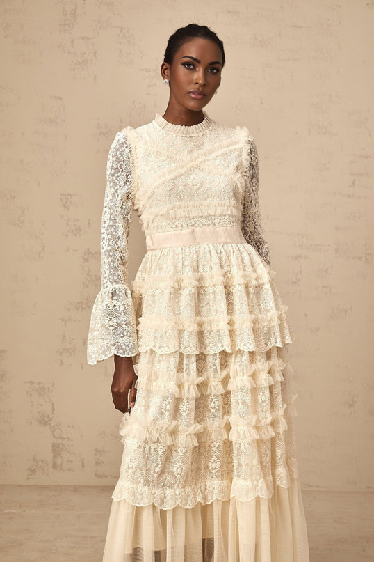 A long flowy maxi dress in neutral tones featuring lace panels and ruffled tulle details