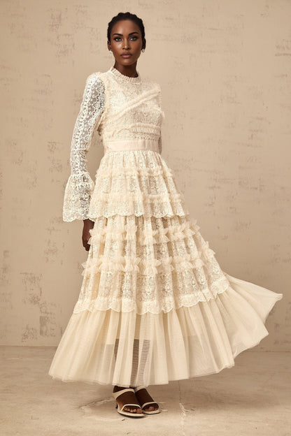 A long flowy maxi dress in neutral tones with lace panels and ruffle details made from tulle fabric