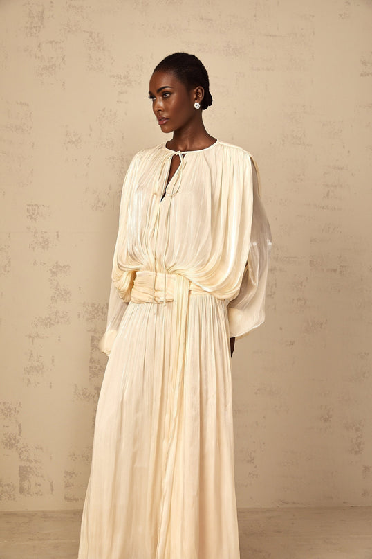 A long flowy maxi dress with pleated ruffles in a neutral color featuring a feminine silhouette and elegant design
