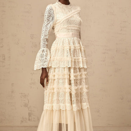 A long flowy neutralcolored maxi dress with lace panels and tulle ruffles