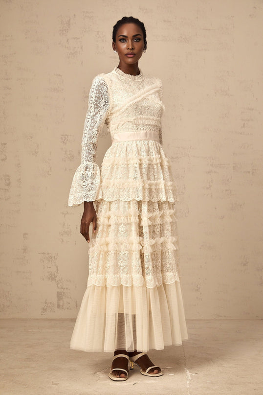 A long flowy neutralcolored maxi dress with lace panels and tulle ruffles