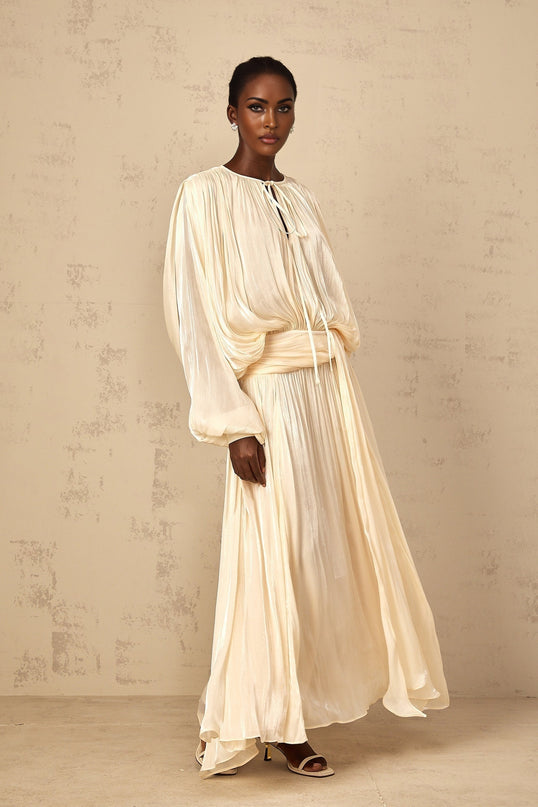 A long neutral colored maxi dress with pleated ruffles and a feminine silhouette called the Eugenie