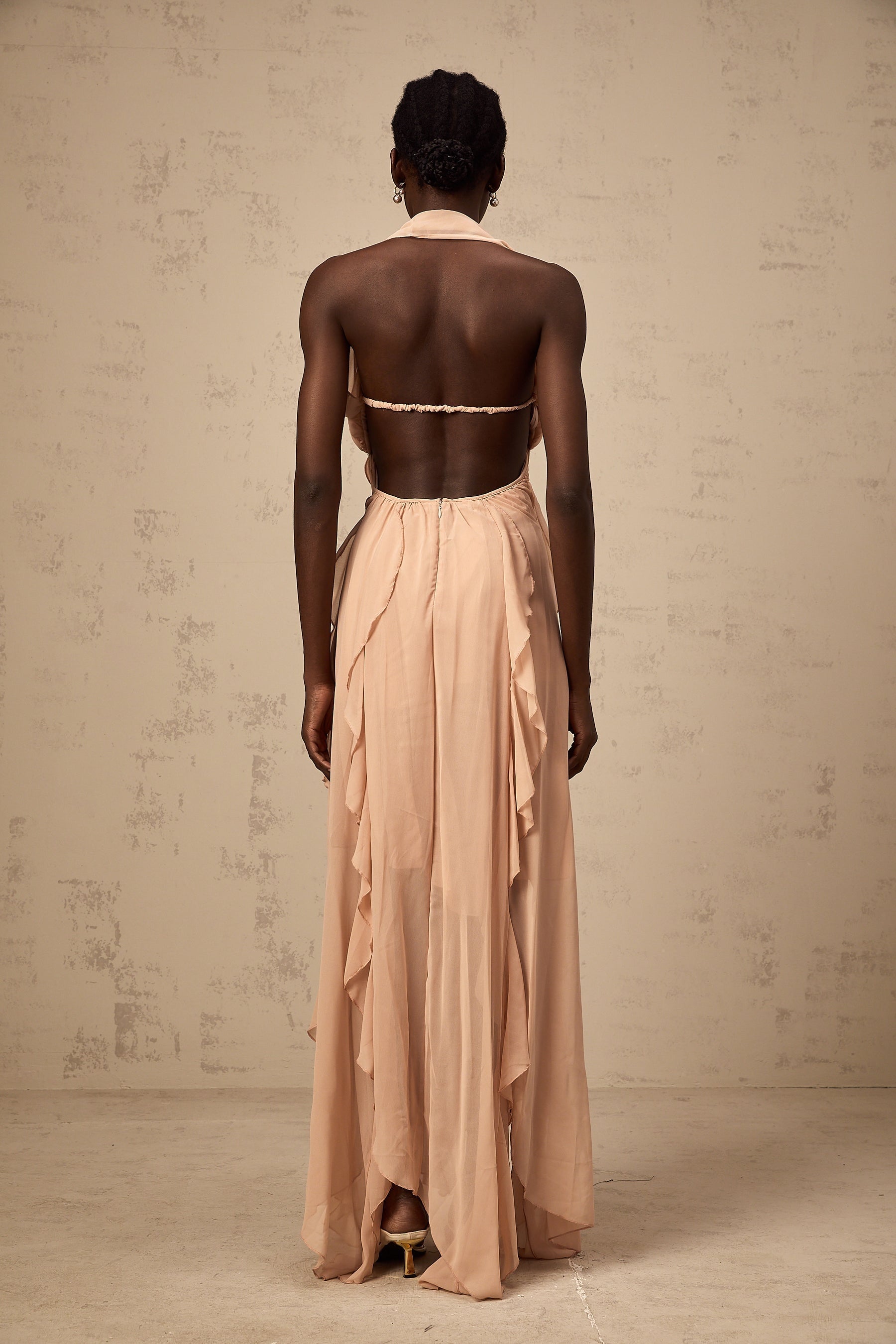 A long pink chiffon maxi dress with a halter neck and ruffle details worn by a model standing against a plain background