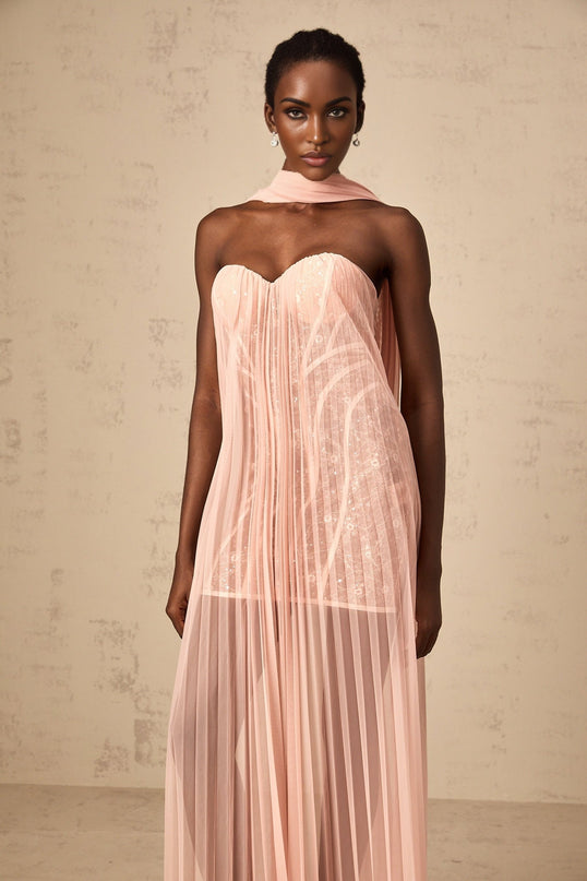 A long pink maxi dress with a pleated tulle skirt and ribbon design details worn by a model standing against a plain background