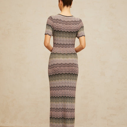 A long pink maxi dress with a wavy crochet knit pattern throughout featuring a fitted bodice and flowing skirt