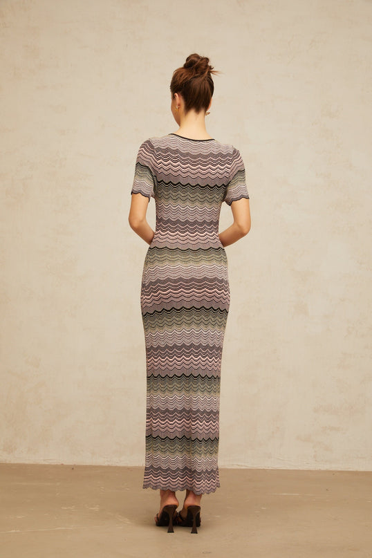 A long pink maxi dress with a wavy crochet knit pattern throughout featuring a fitted bodice and flowing skirt