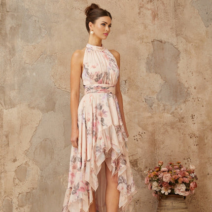 A long pink maxi dress with an asymmetrical hemline featuring a floral print pattern worn by a model against a plain background
