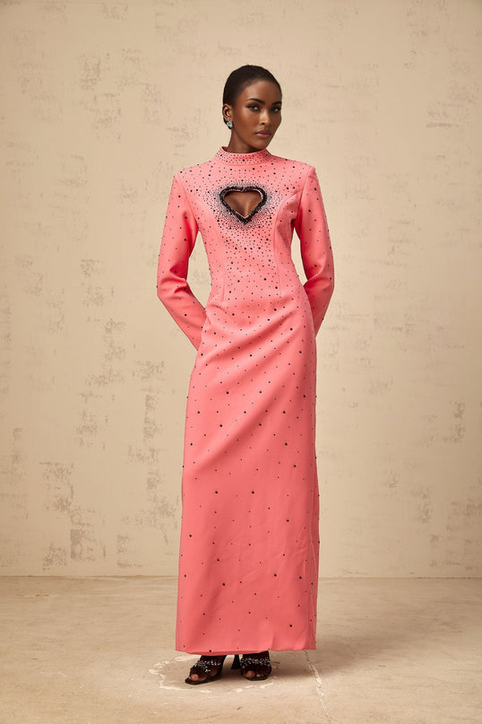 A long pink maxi dress with heart shaped cutouts and embellishments featuring a feminine silhouette and delicate details