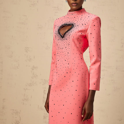 A long pink maxi dress with heart shaped cutouts and embellishments featuring a flowy silhouette and romantic design