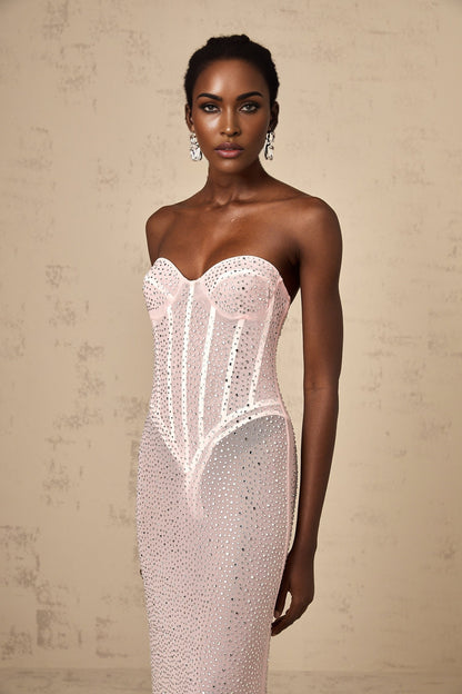 A long pink maxi dress with rhinestone embellishments and sheer elements worn by a model against a plain background