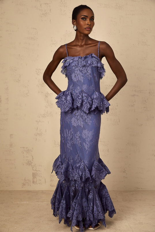 A long purple maxi dress with floral lace pattern and ruffled details worn by a model standing in a relaxed pose