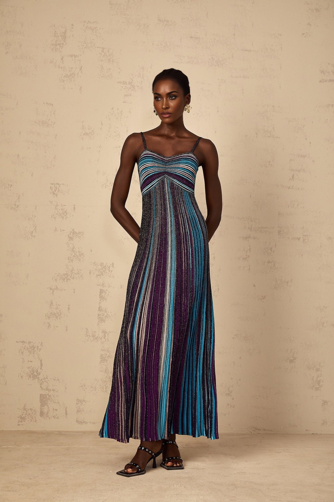 A long purple maxi dress with horizontal sequin stripes throughout the knitted fabric worn by a woman