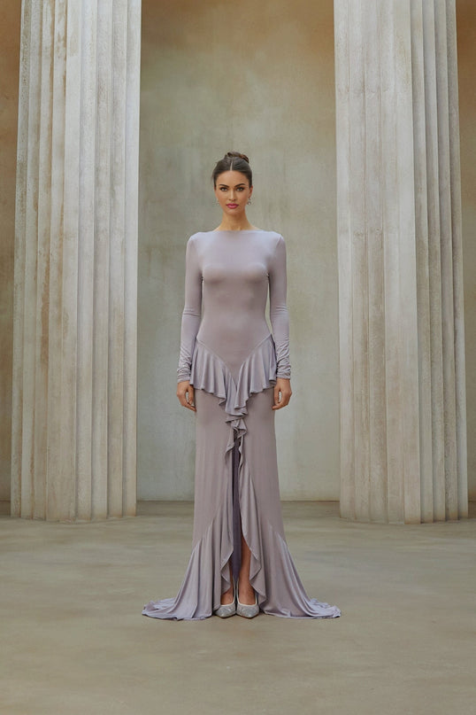 A long purple maxi dress with ruffle details and a front slit worn by a model against a plain background