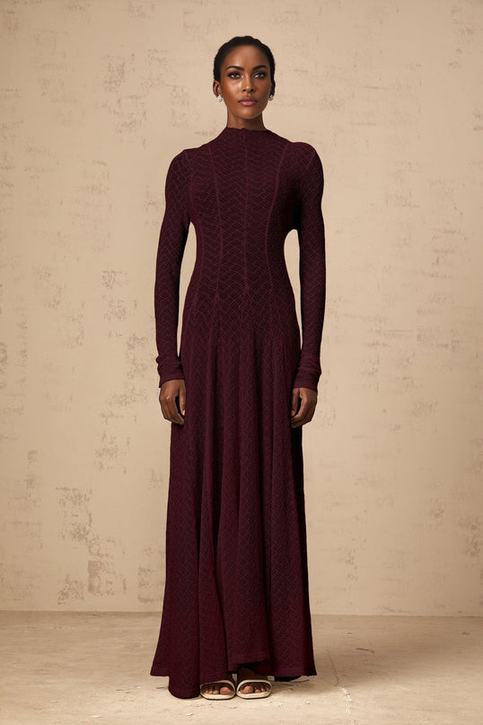 A long red lace maxi dress with a wavy pattern design worn by a model standing against a plain background