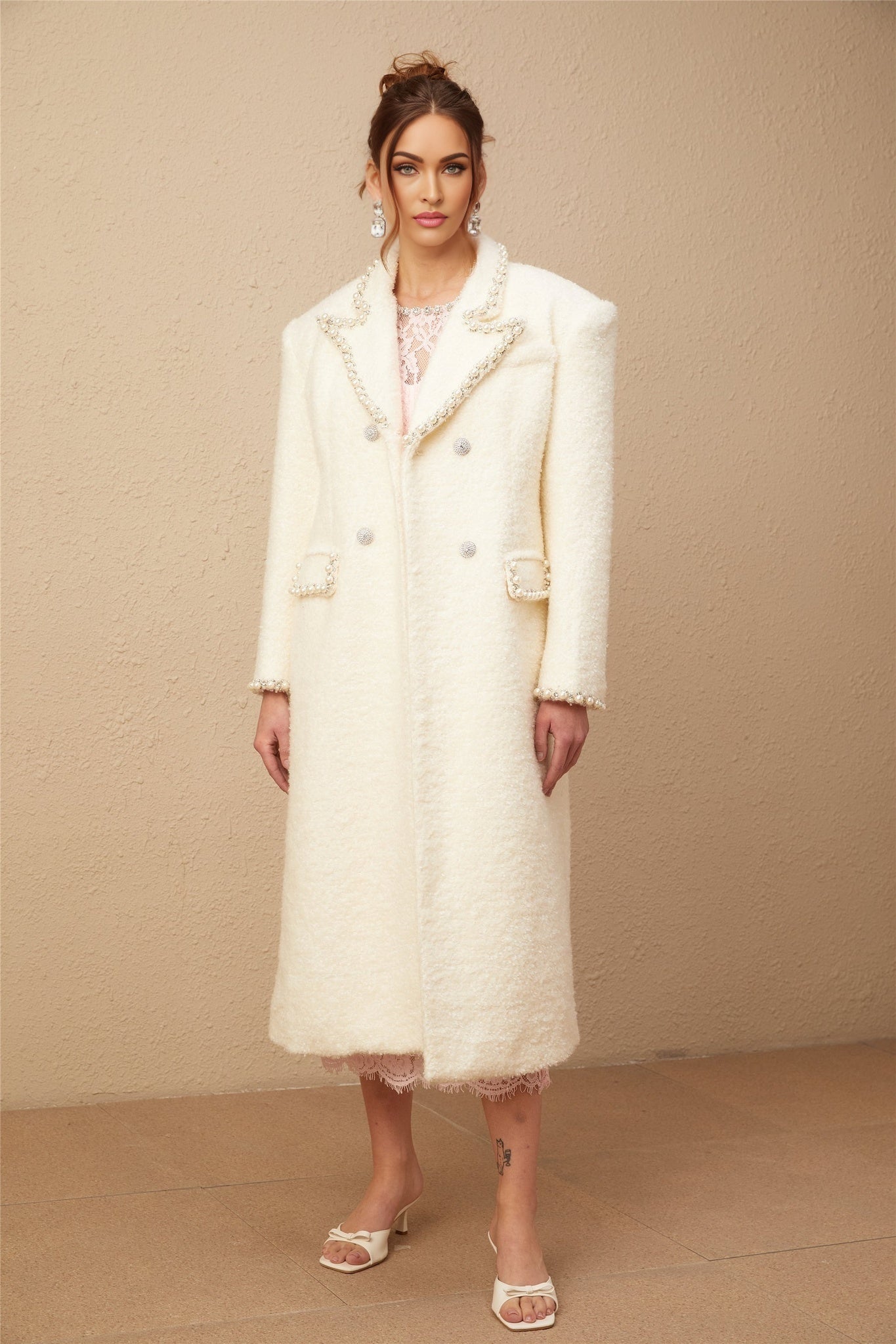 A long tweed coat made of Isotta wool in a light color featuring faux pearl embellishments throughout the fabric