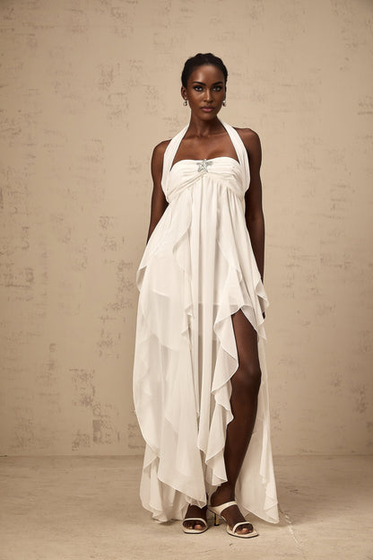 A long white chiffon maxi dress with a halter neck and ruffle details worn by a model standing against a plain background