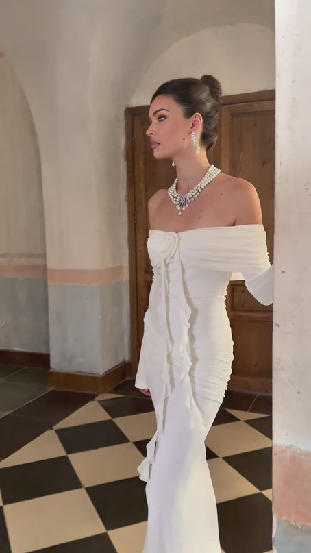 A long white knit dress with glittery floral appliques scattered across the fabric featuring a maxi length design