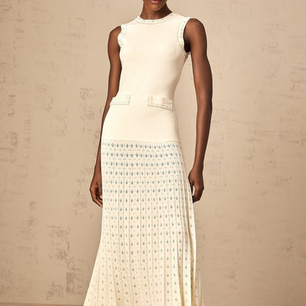 A long white knitted maxi dress with faux pearl embellishments worn by a model standing against a plain background