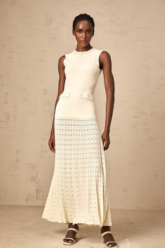 A long white knitted maxi dress with faux pearl embellishments worn by a model standing against a plain background