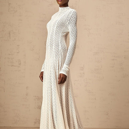 A long white lace maxi dress with a wavy pattern design worn by a model standing in a neutral setting