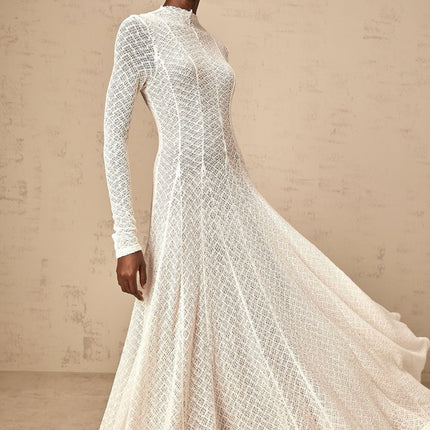 A long white lace maxi dress with a wavy pattern worn by a model standing against a plain background