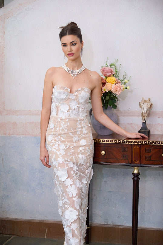 A long white maxi dress with a corset bodice featuring floral appliqué details named Brigitte