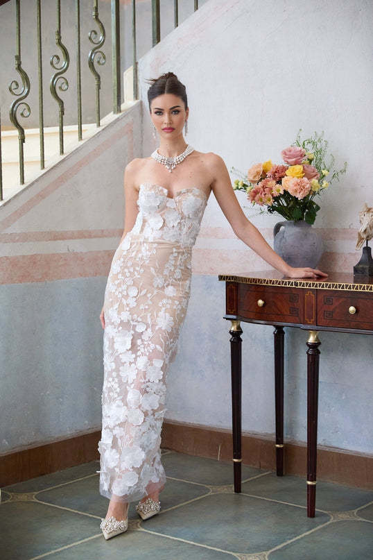 A long white maxi dress with a corset bodice featuring floral appliqué details named Brigitte