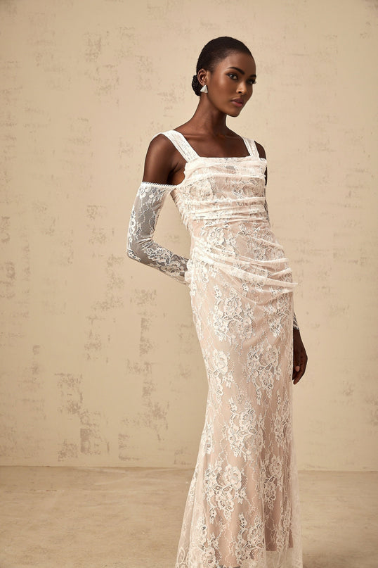 A long white maxi dress with a corset bodice featuring ruched floral lace detailing and a flowing skirt