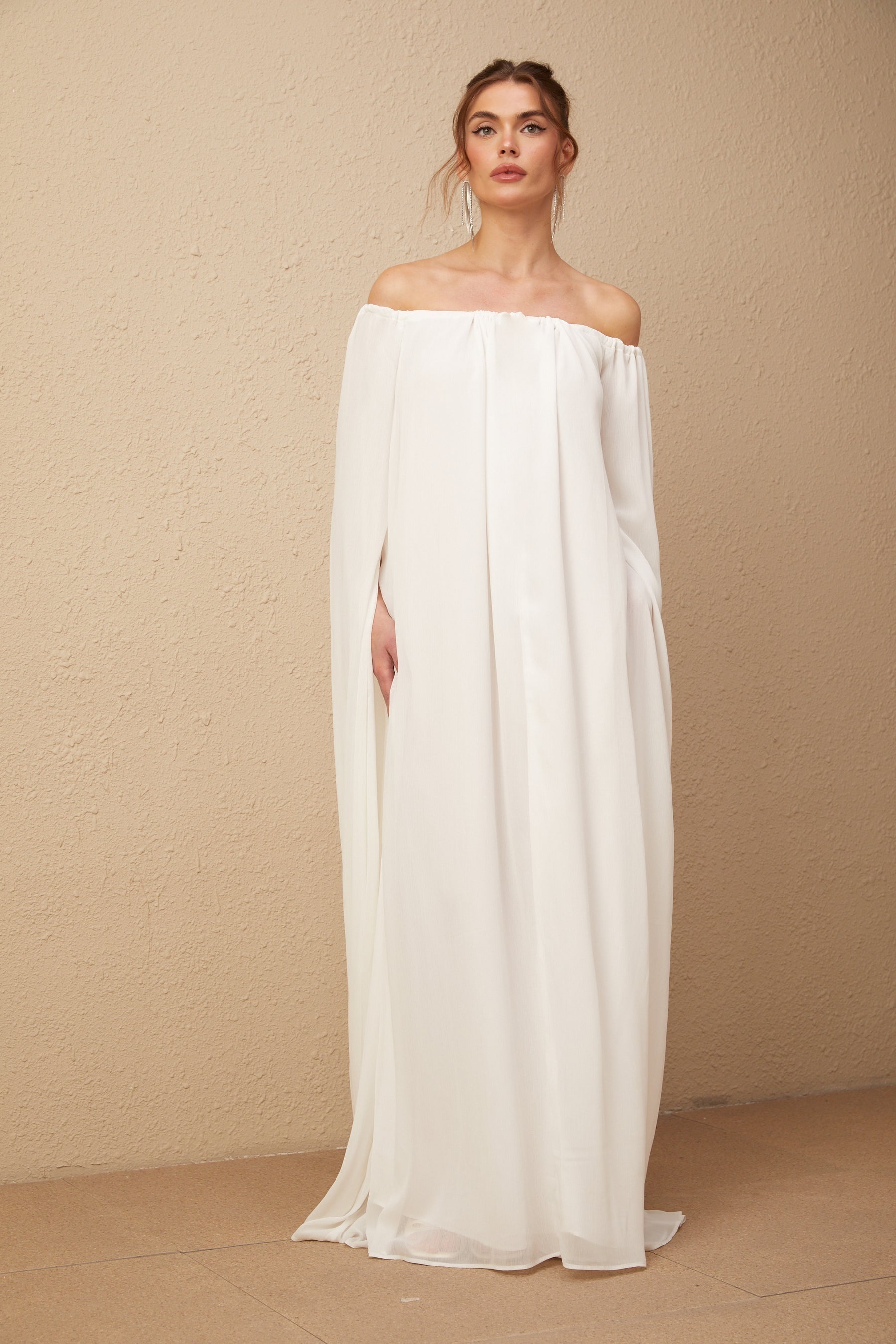 A long white maxi dress with a flowing tulle skirt and capelike draped design on the upper body