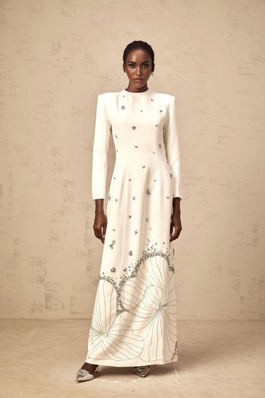 A long white maxi dress with a lotus flower pattern featuring embellishments and details inspired by the Daphne design