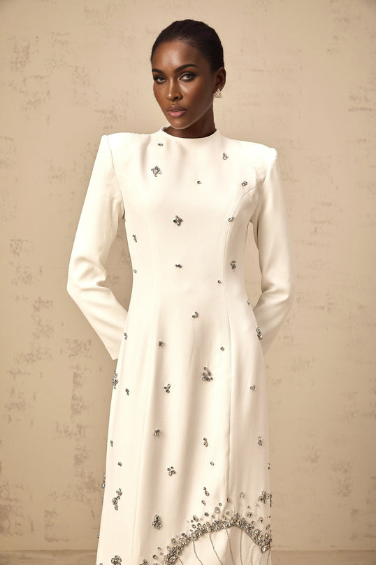 A long white maxi dress with lotus flower embellishments adorning the fabric