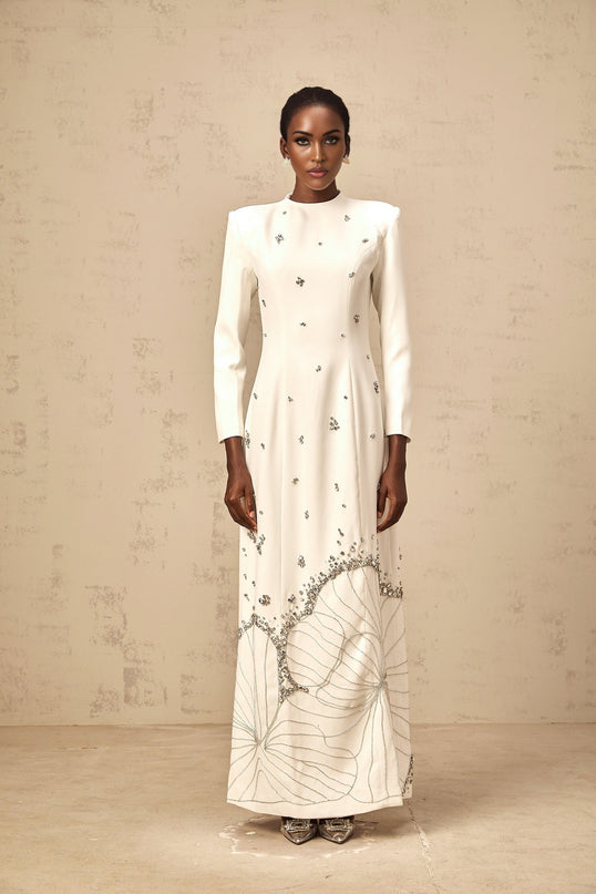 A long white maxi dress with lotus flower embellishments and a flowing silhouette named Daphne