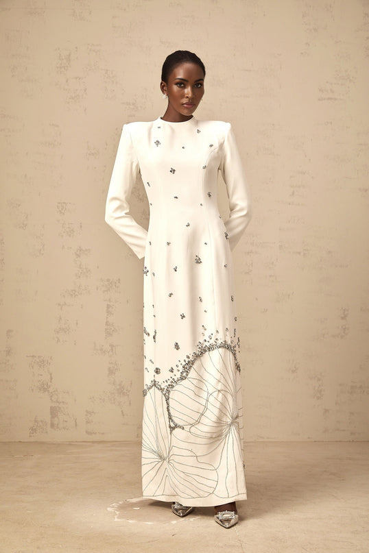 A long white maxi dress with lotus flower embellishments and a flowing silhouette
